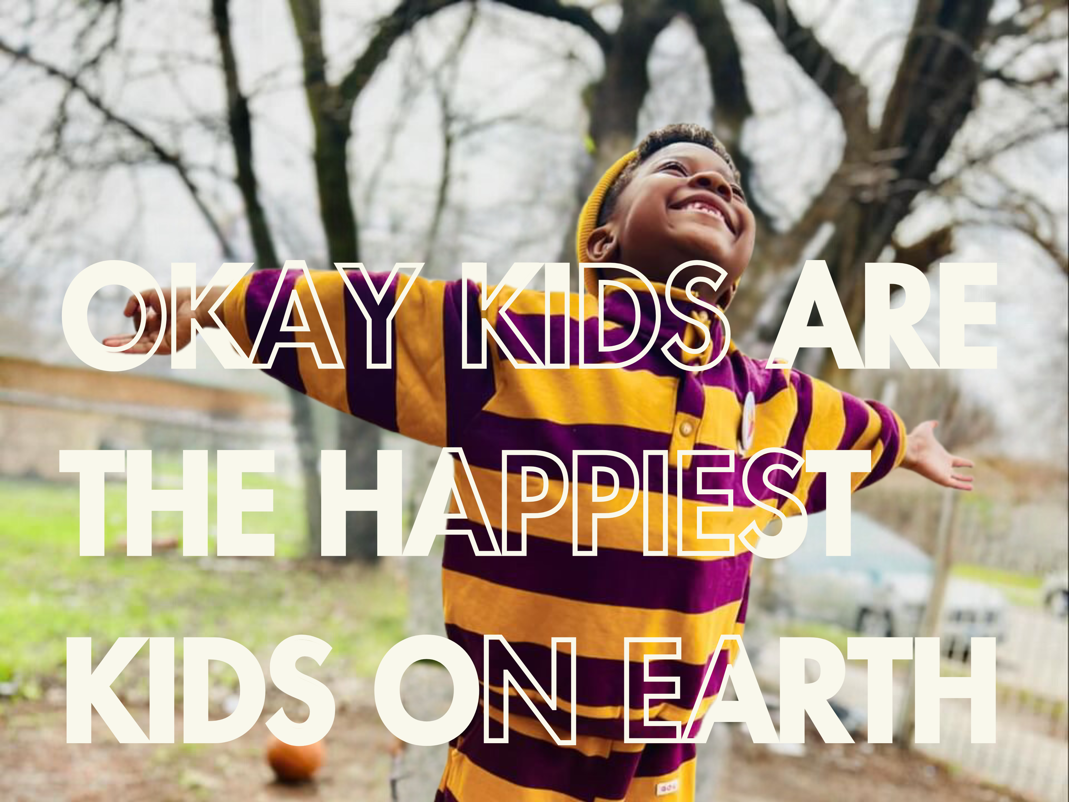 second slideshow image of young black child stands with arms wide open with huge smile on their face. Text reads "Okay Kids are the happiest kids on earth" and promotes our colorful kids clothing line. The child wears a matching top and bottom sweatsuit with gold and maroon stripes and snap buttons on the neck. 