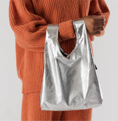 model wearing orange set holding shiny metallic sliver reflective reusable bag mini small baby baggu 100% recycled nylon 