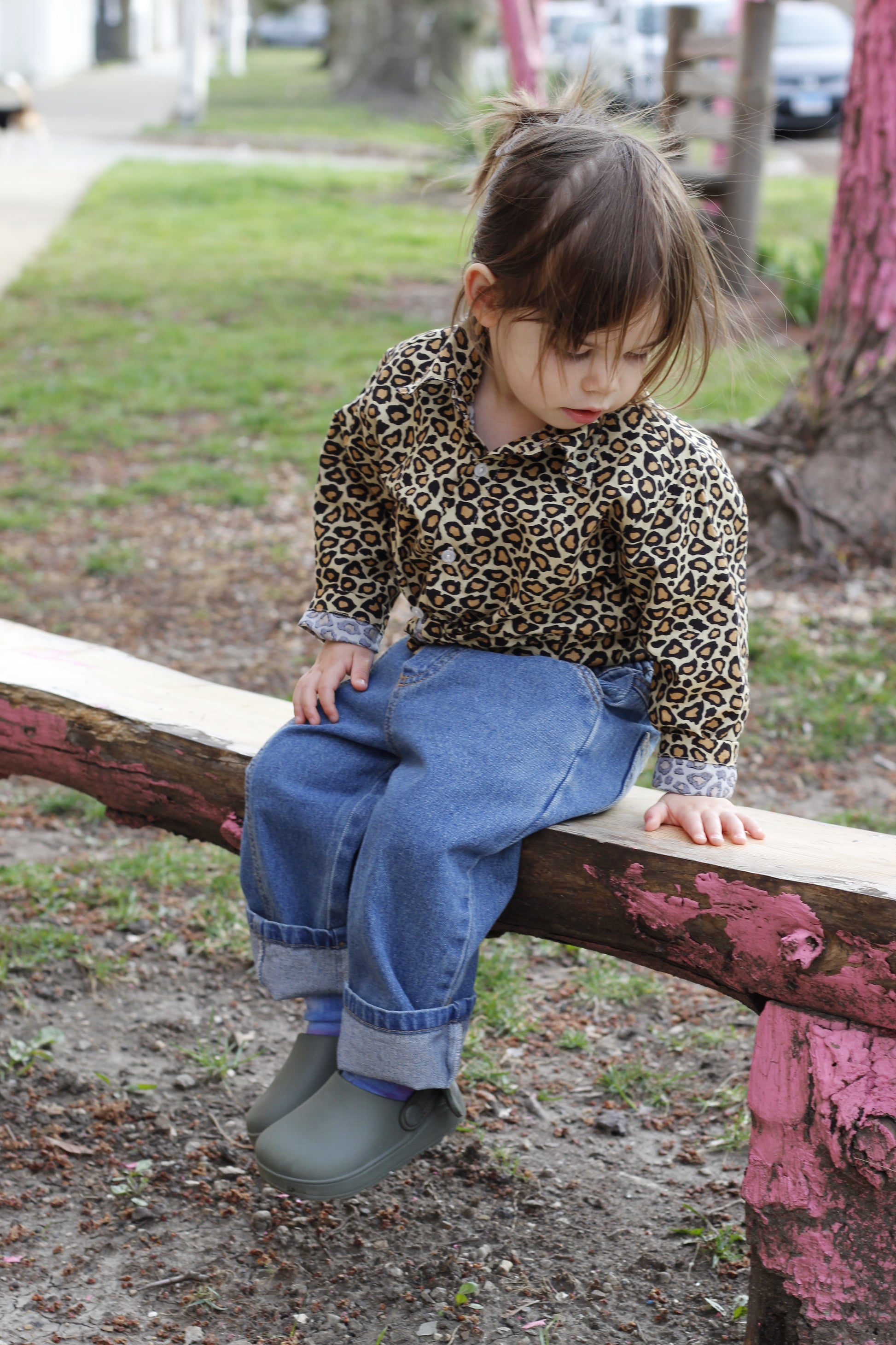 young child wears leopard print shirt and kids peekaboo pocket denim blue jeans pants trousers bottoms detailed pocket leg seam detail elastic waist stretchy back pockets sitting on pink wood bench