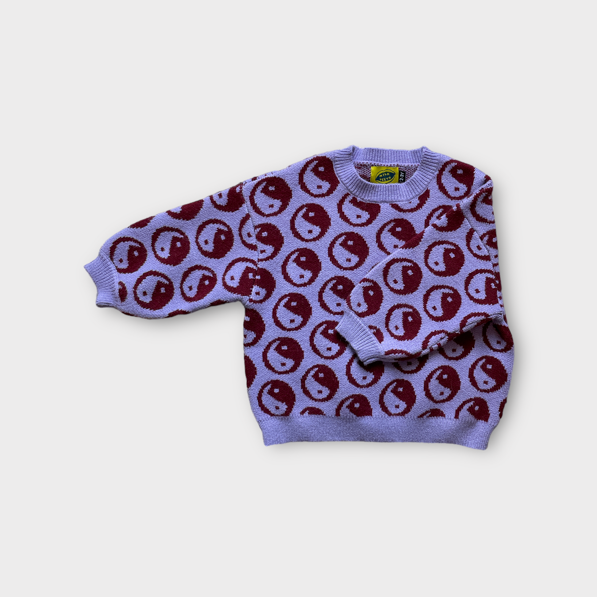 violet kids sweater covered with dark ying yang symbols the right sleeve is folded to show pattern on sleeve
